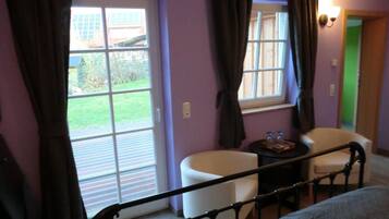 A room with a bed, a small table with a tray, two chairs, and a window with curtains.