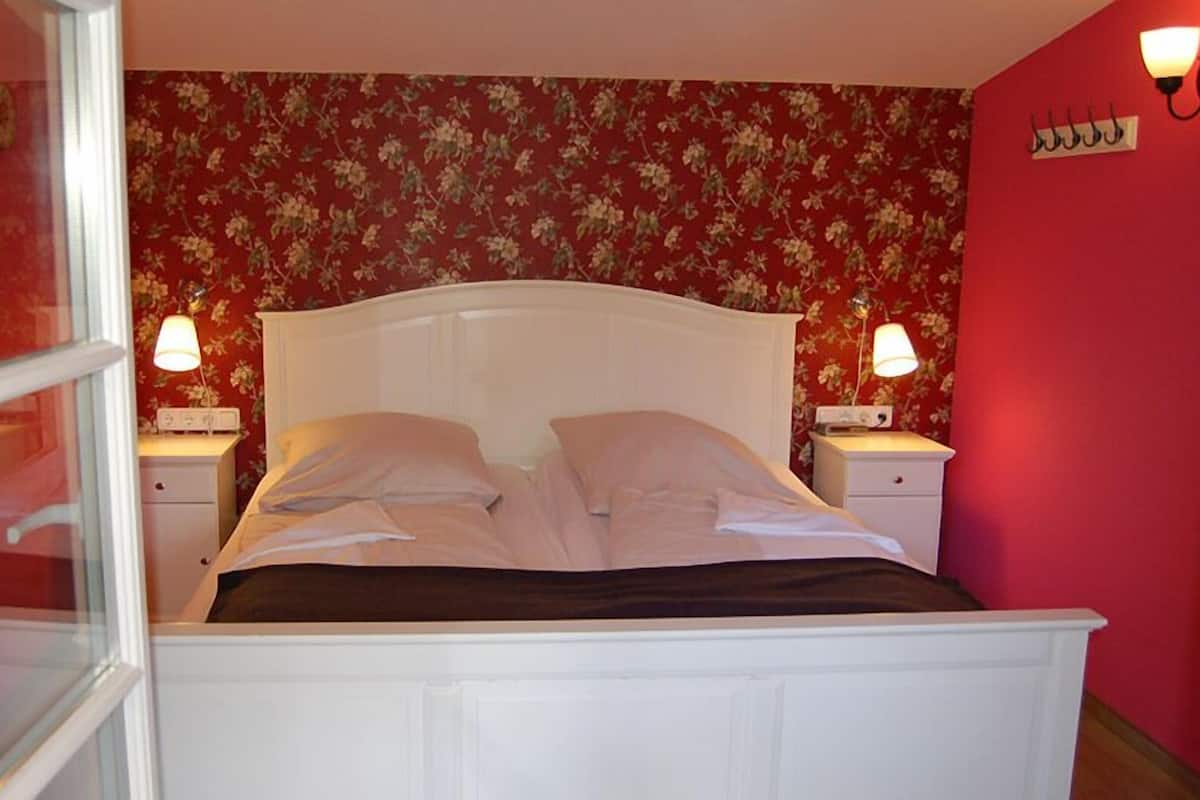 A bedroom with a white bed, floral wallpaper, and bedside lamps.
