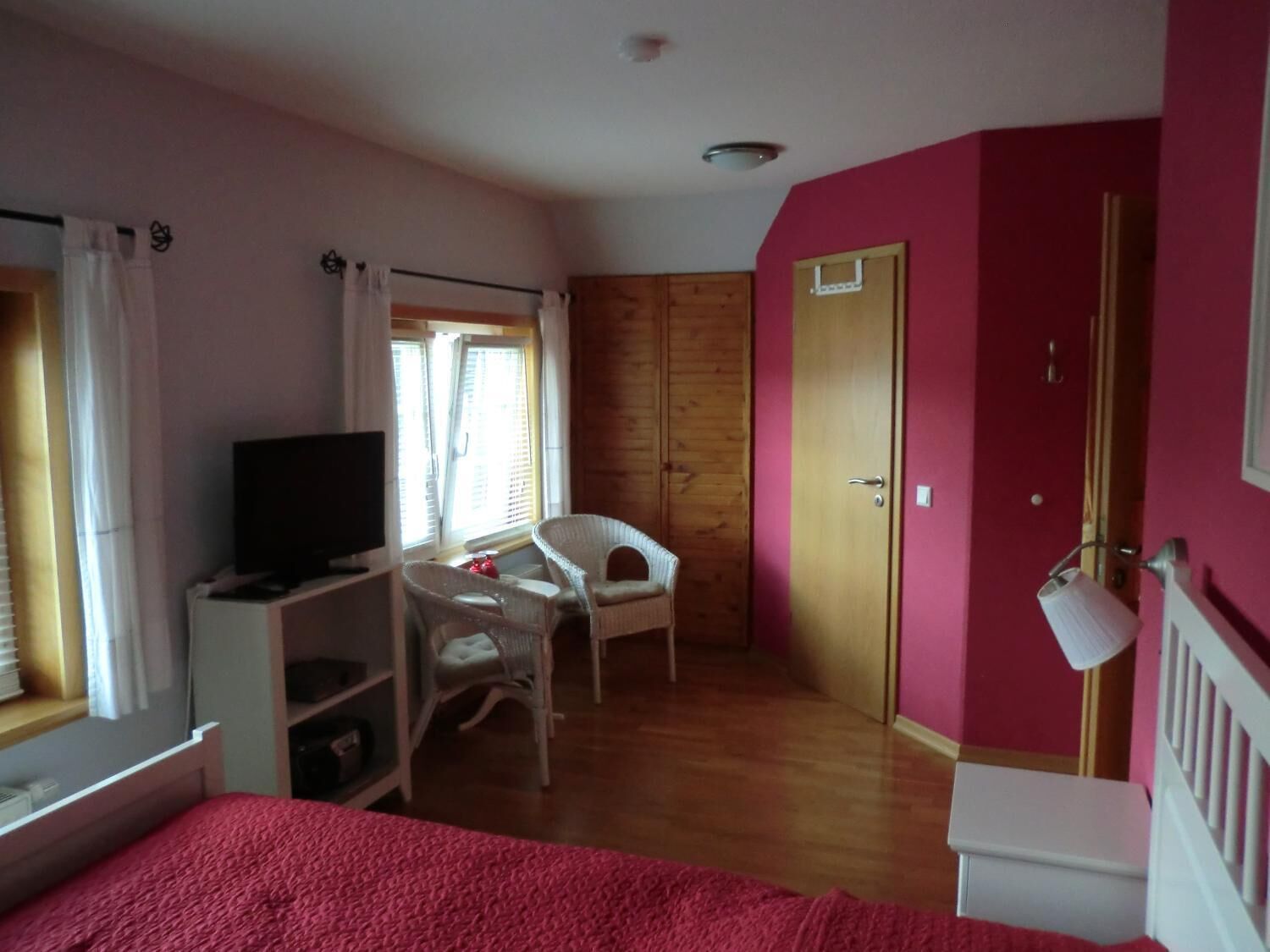Una habitación con cama, televisión, silla, armario de madera y puerta.