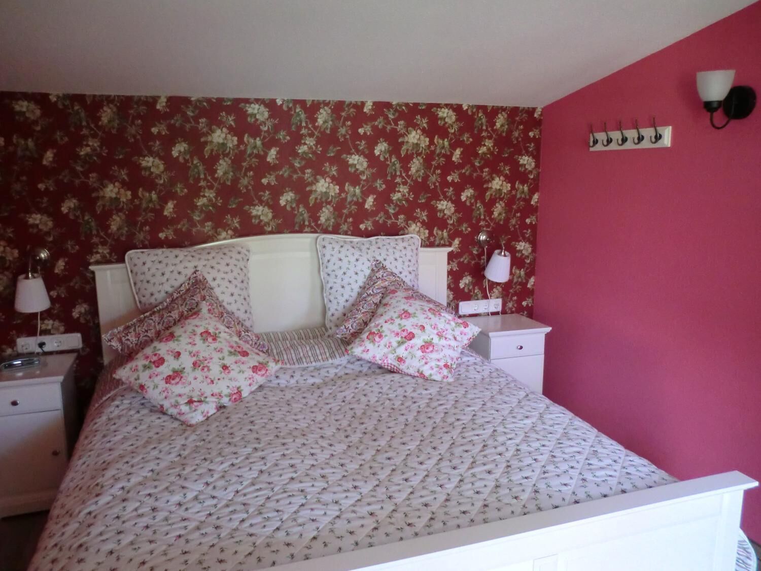 Een slaapkamer met een bloemenprint bedsprei, een wit hoofdeinde en twee bedlampen.