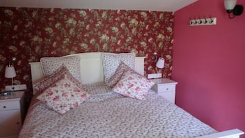 Un dormitorio con colcha de estampado floral, cabecera blanca y dos lámparas de noche.