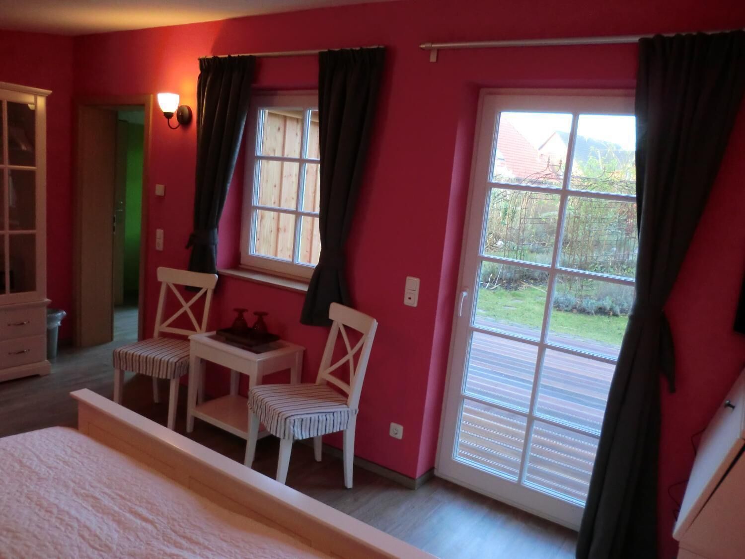 Un dormitorio con cama, dos sillas, una mesita y un ventanal con cortinas.
