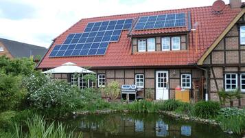 Una casa con paneles solares en el techo, un estanque y una zona de barbacoa.