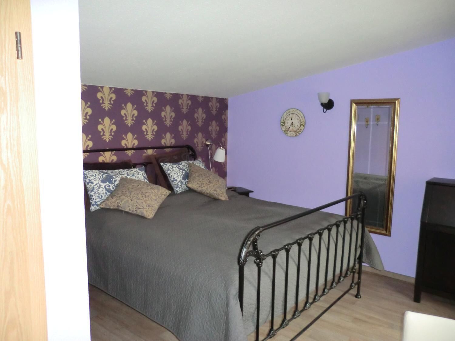 Ein Schlafzimmer mit Bett, Spiegel, einer Uhr und einer Lampe.