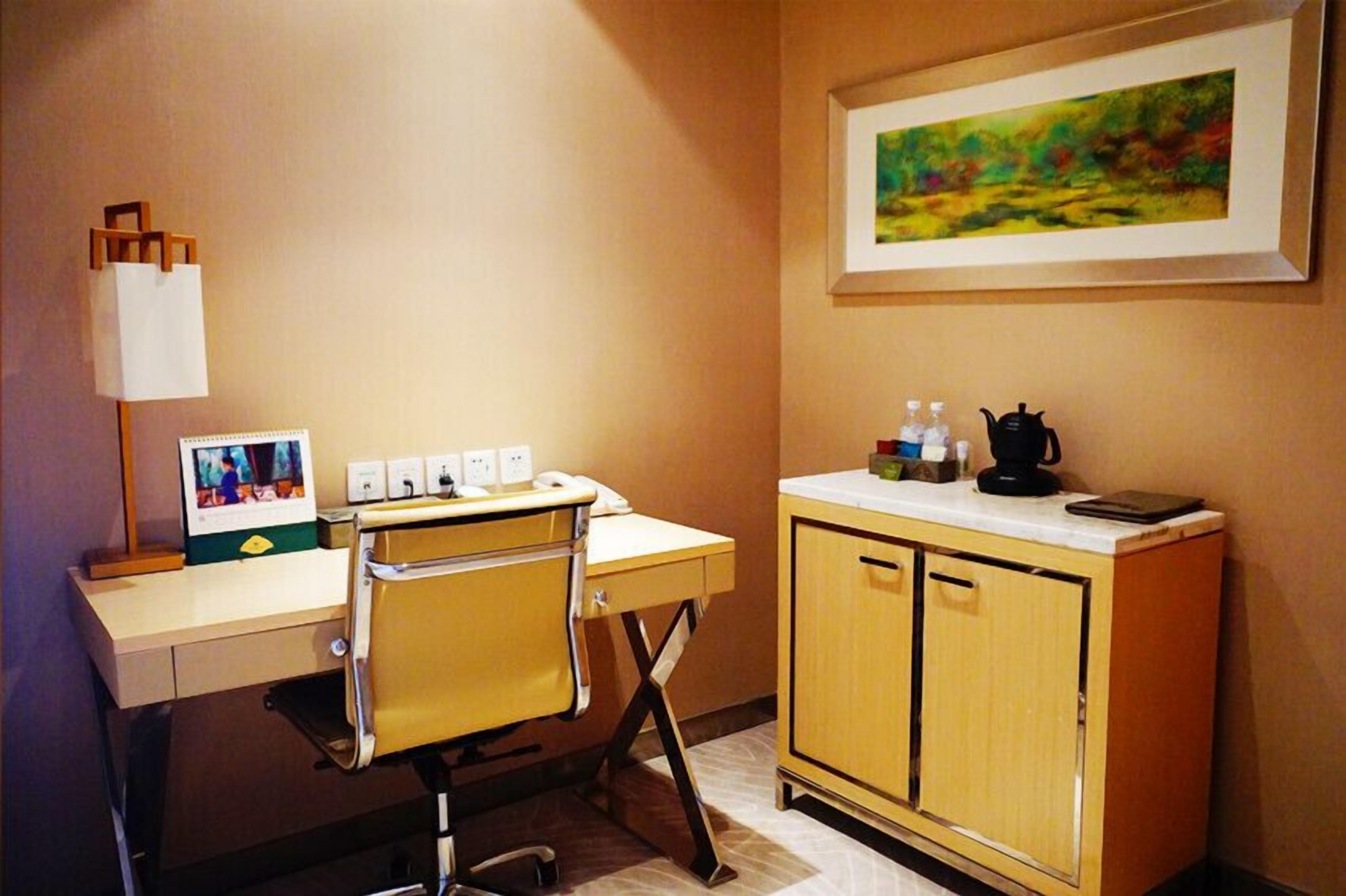 A room with a desk, chair, and a cabinet with a painting above it.