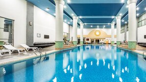 Une piscine intérieure à l’eau claire, entourée de chaises longues et dotée d’un sol carrelé.