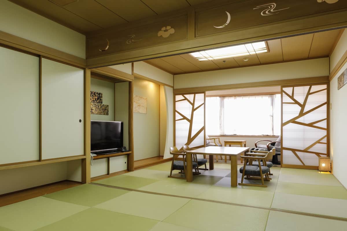 Une pièce de style japonais traditionnel, avec un sol recouvert de tatamis, un téléviseur et un coin repas comprenant une table basse et des chaises.