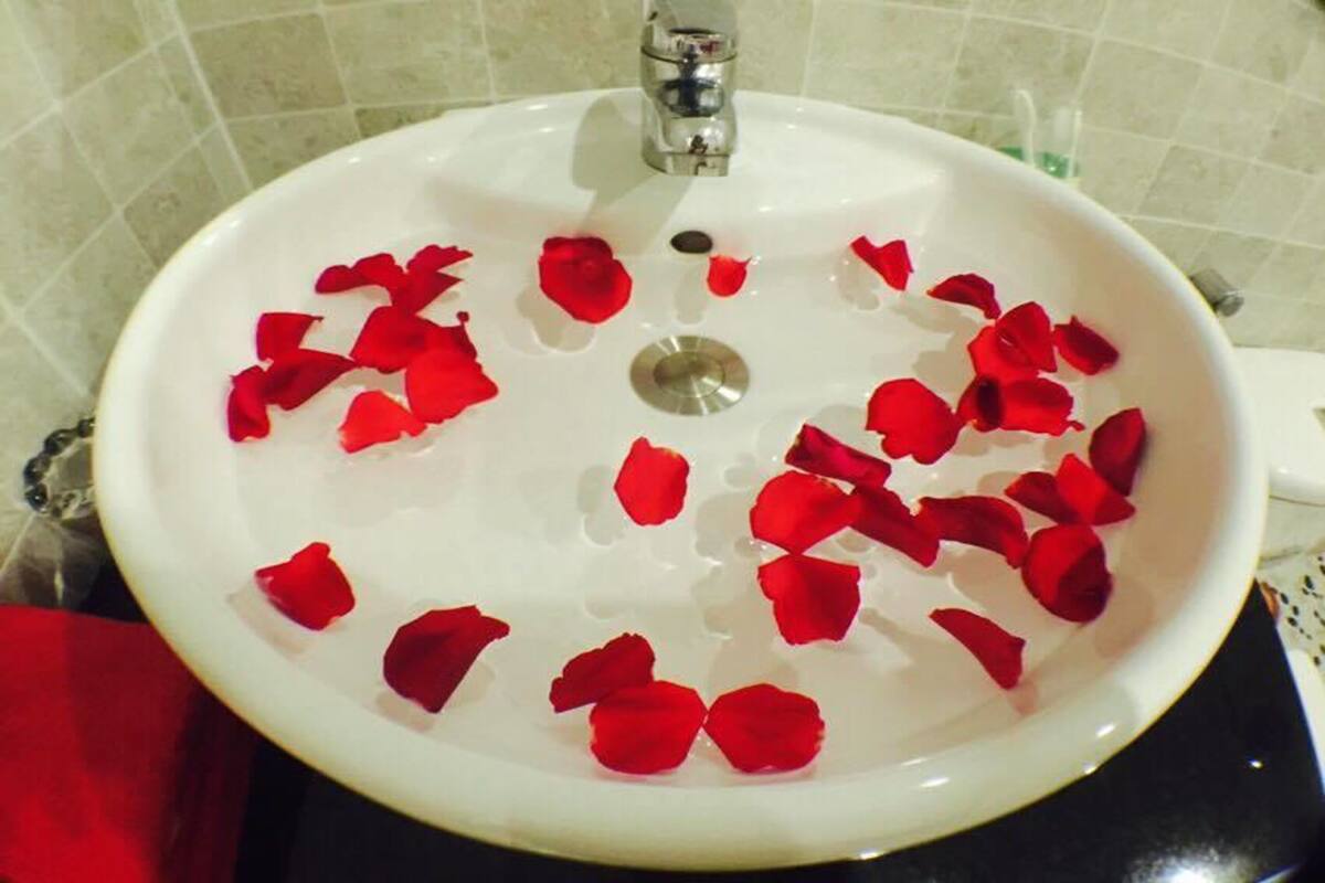A white bathroom sink with rose petals floating in the water.
