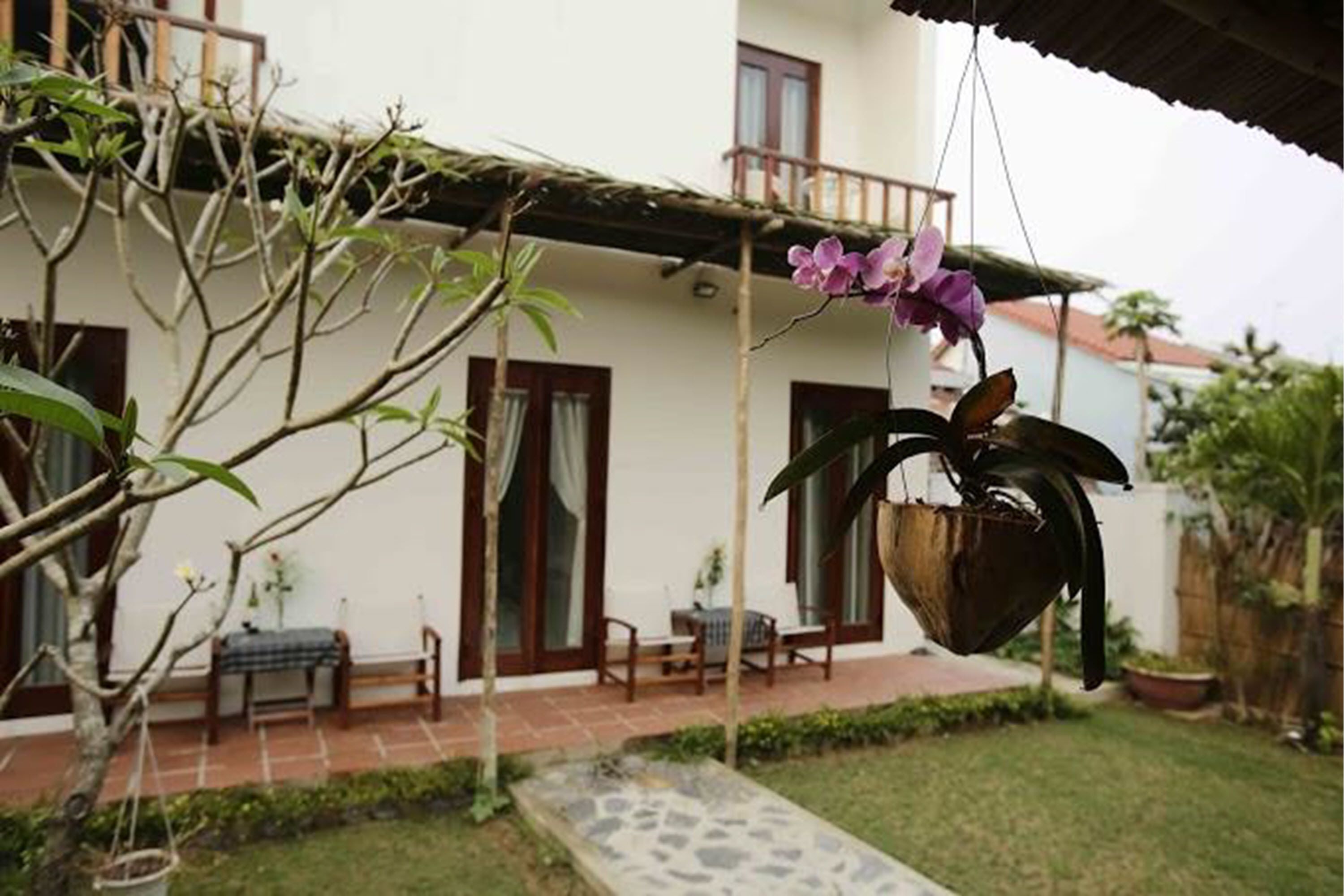 Una casa amb un balcó, una orquídia penjant i un petit jardí.