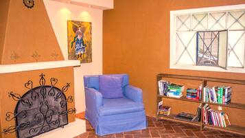 A room with a blue armchair, a bookshelf with books, a painting on the wall, and a decorative metal headboard.