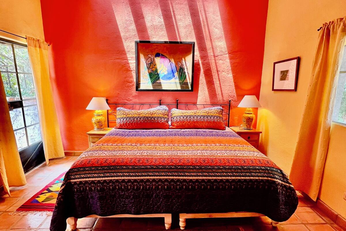 Un dormitorio con una cama grande, techo de madera, un cuadro y vistas por la ventana.