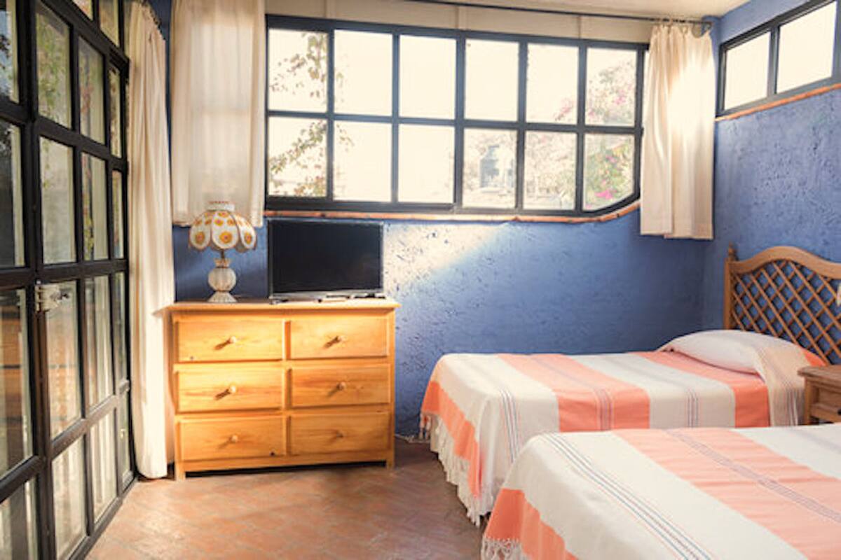 Un dormitorio con cama, cómoda de madera, televisor y ventana con cortinas.