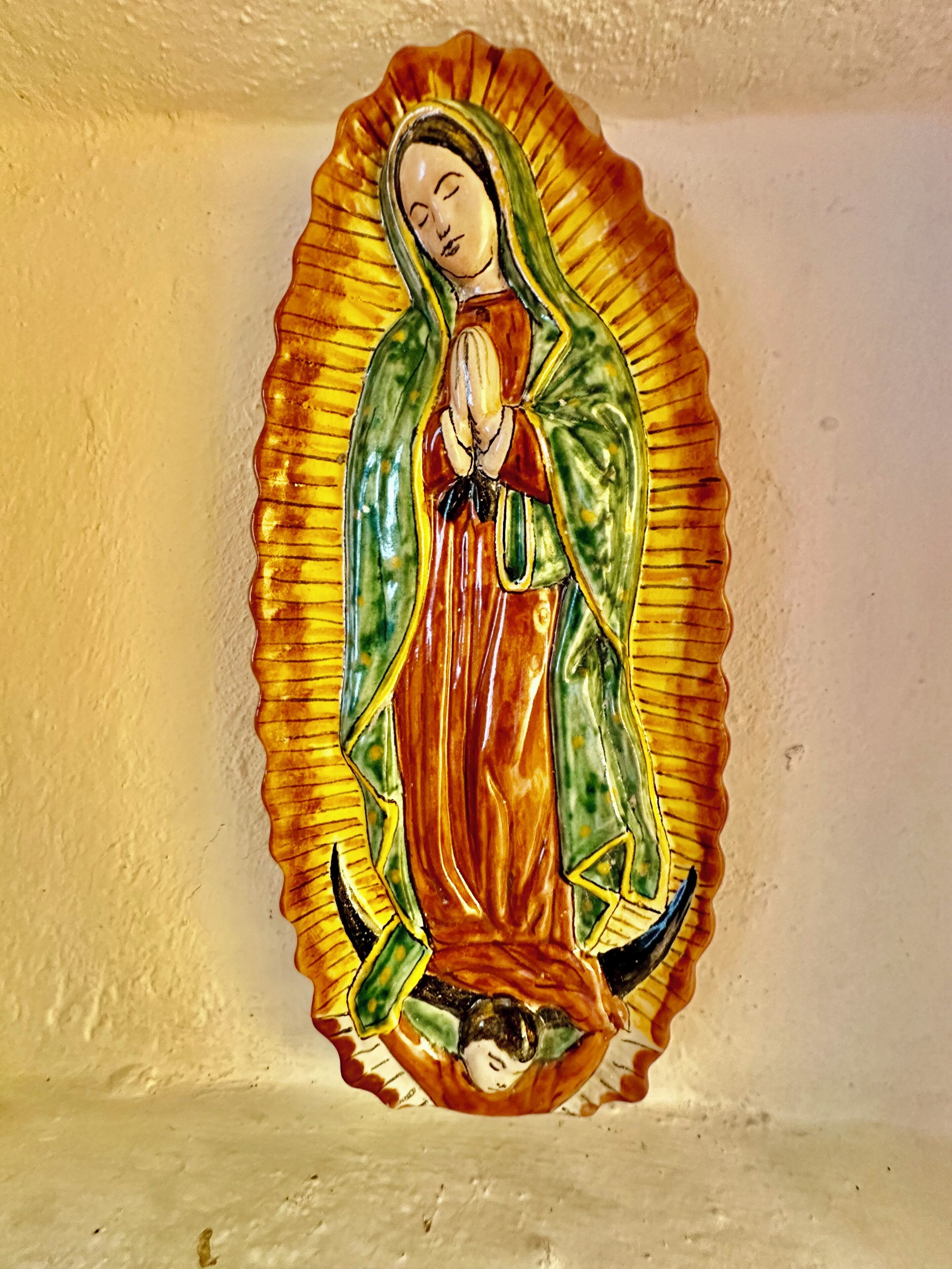 A religious icon with a scalloped frame, depicting a figure in a red robe and green cloak, set against a plain wall.