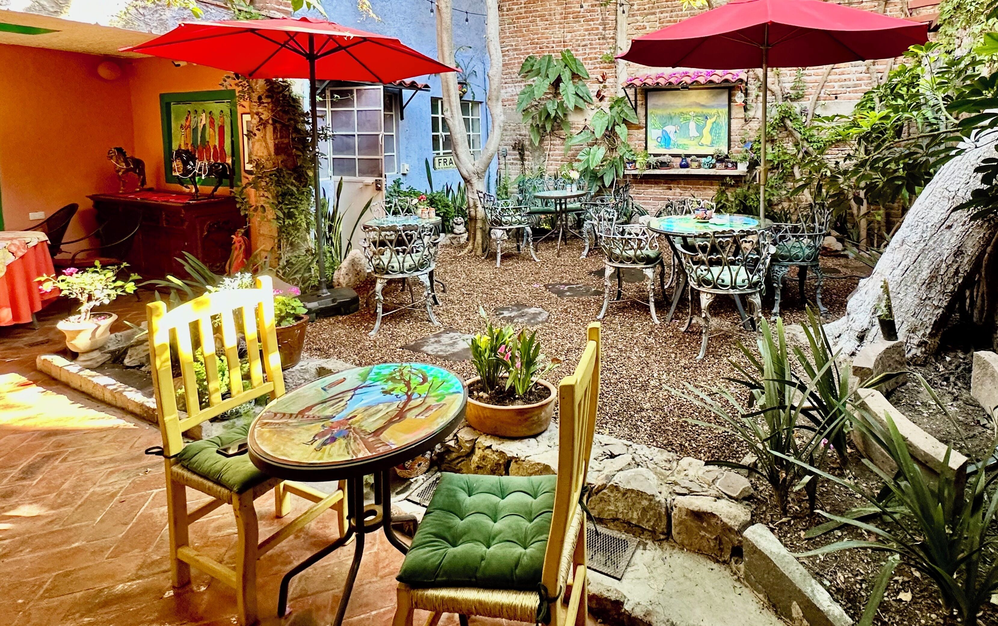 Un patio al aire libre con mesas y sillas, rodeado de plantas en macetas y una pequeña cascada.