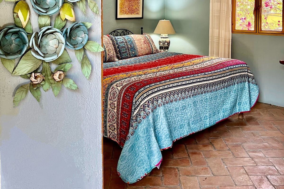 Un dormitorio con cama, decoración en la pared, ventana con cortinas y una lámpara colgante.