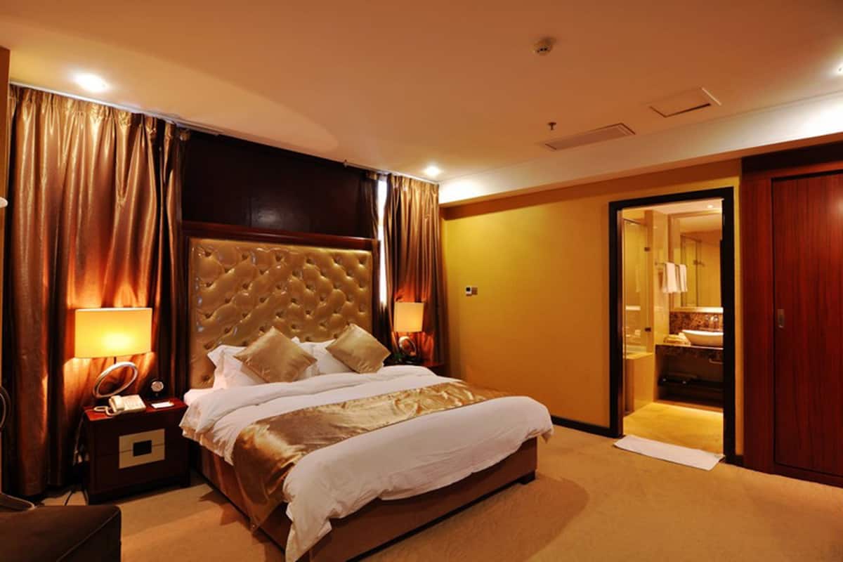 A hotel room with a large bed, two bedside tables with lamps, a wooden headboard, and a bathroom visible through an open door.