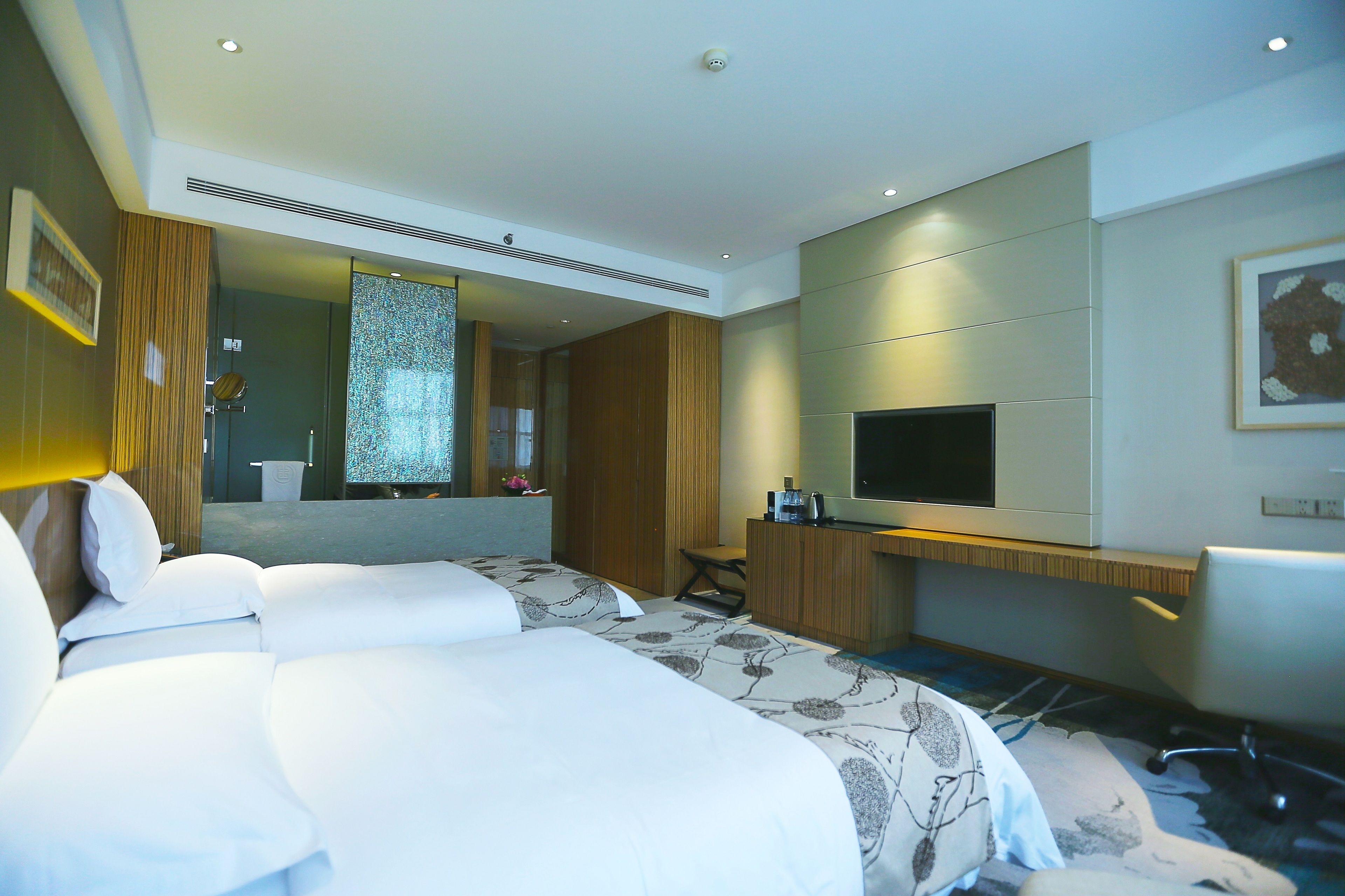 A hotel room with two beds, a TV, a desk, and a large mirror.
