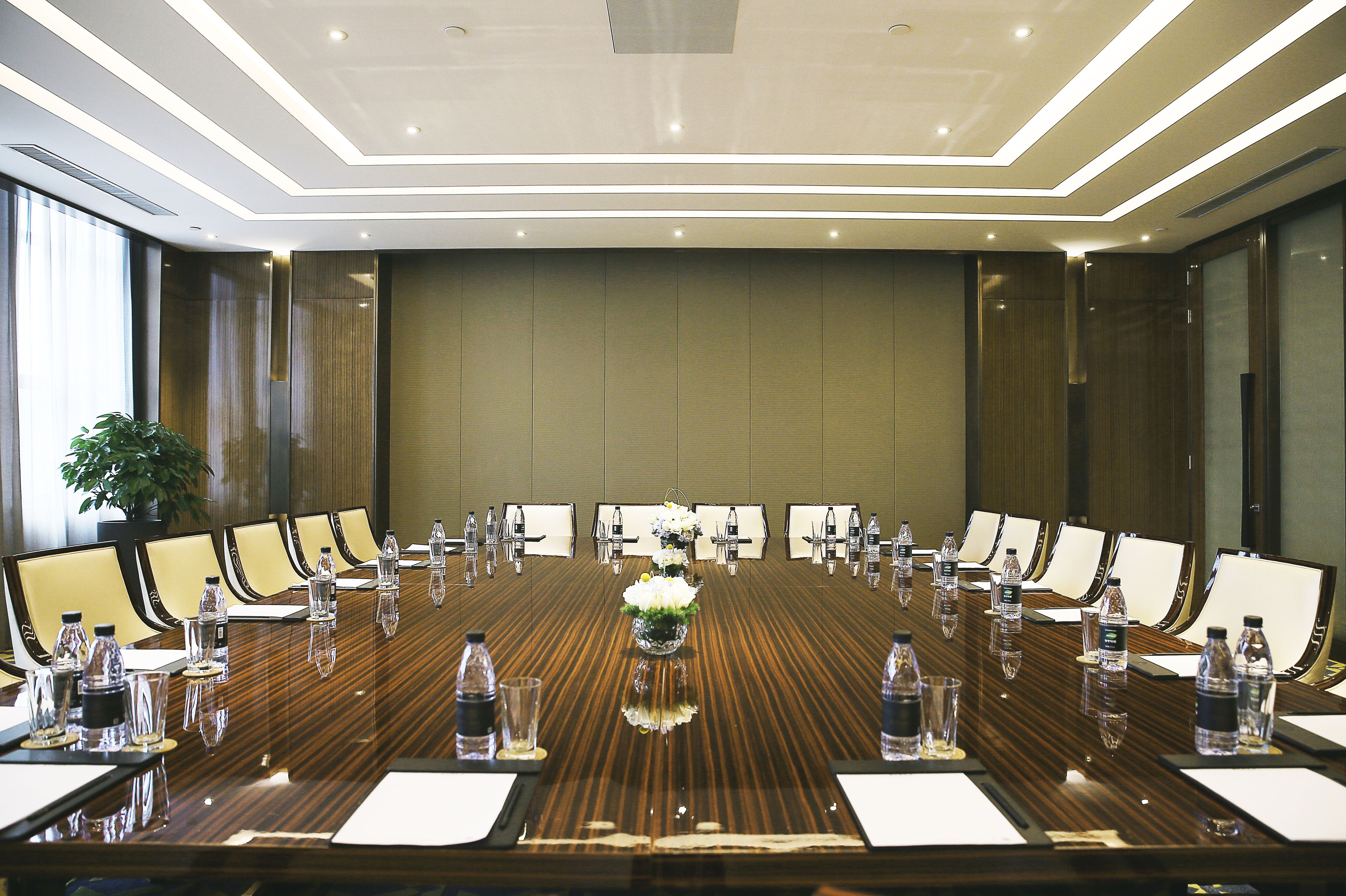 Une salle de conférence avec une longue table, des chaises, des bouteilles d’eau et un arrangement floral au centre.