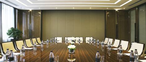 Une salle de conférence avec une longue table, des chaises, des bouteilles d’eau et un arrangement floral au centre.