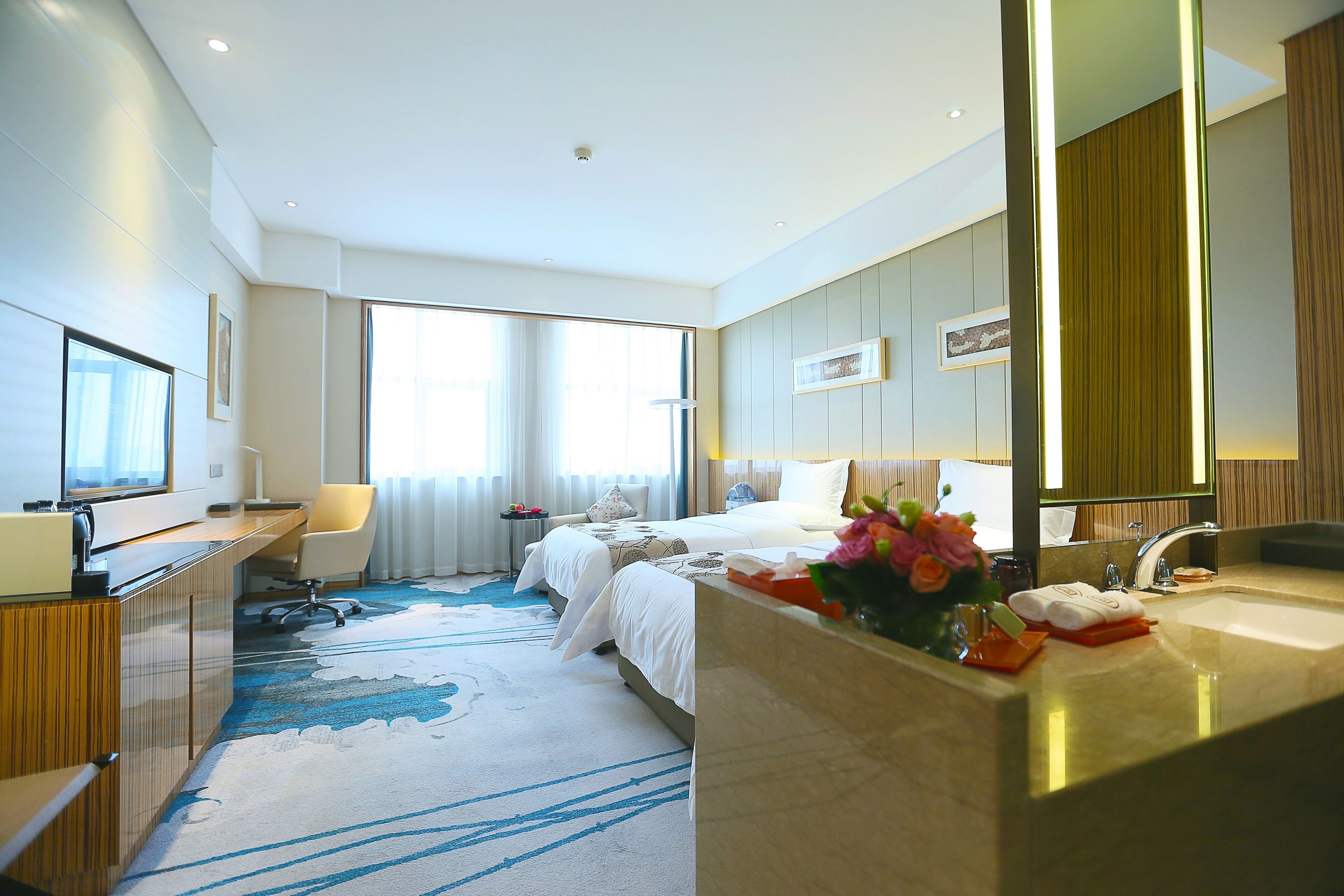 A hotel room with a large bed, a desk, a bathroom with a sink, and a large window.