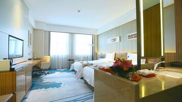 A hotel room with a large bed, a desk, a bathroom with a sink, and a large window.