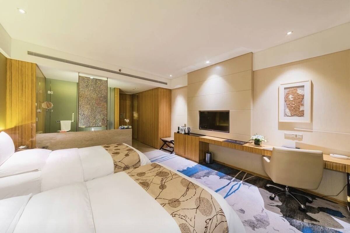 Una habitación de hotel moderna con una cama grande, un escritorio con computadora, un televisor y un espejo amplio.