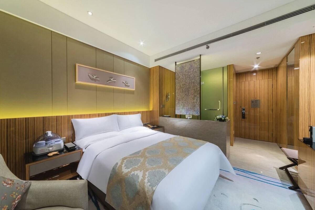 Una habitación de hotel moderna con una cama grande, una mesita de noche con lámpara, un espejo y un armario de madera.