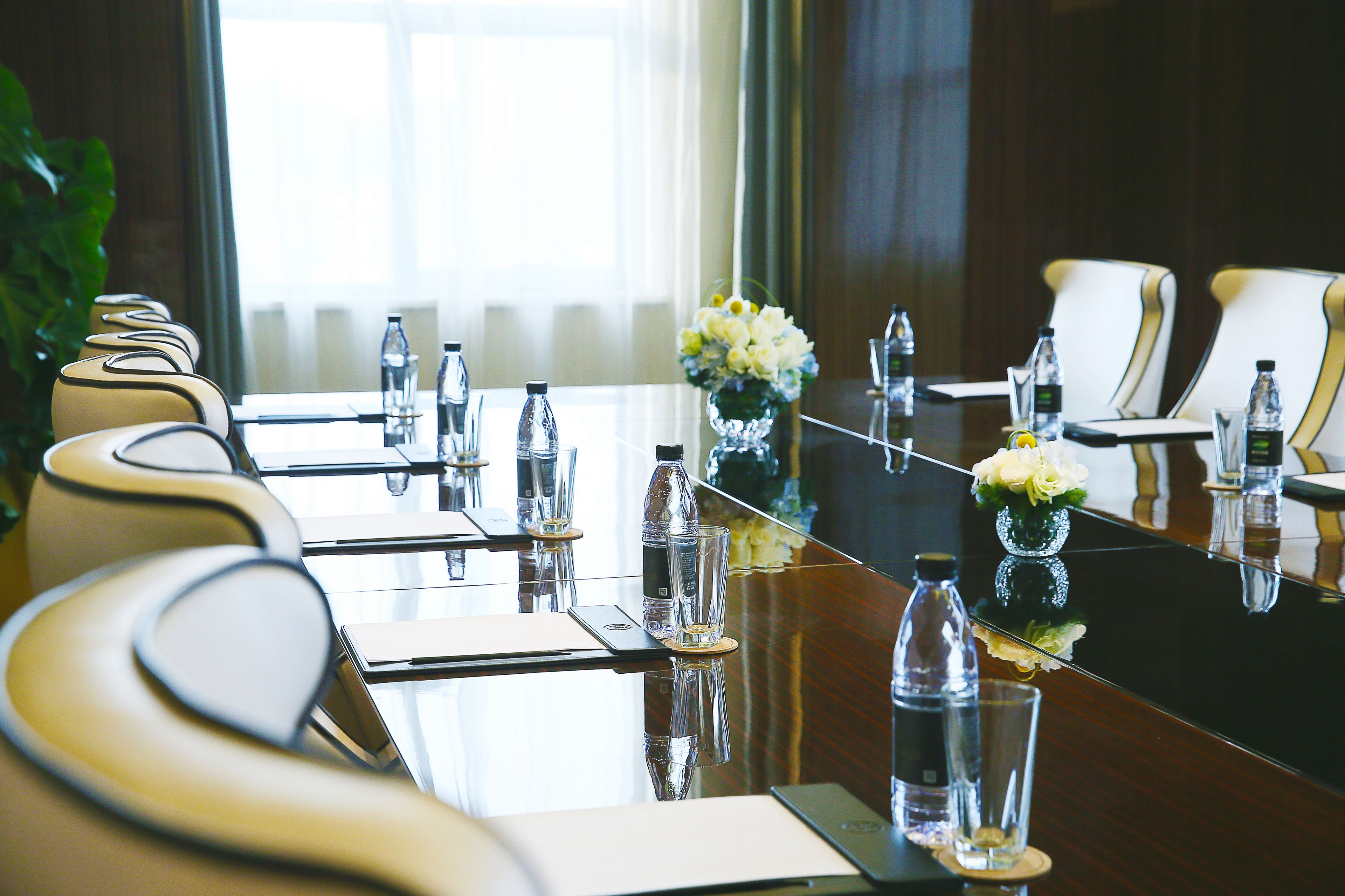 Una mesa de conferencias con sillas, botellas de agua y jarrones con flores.