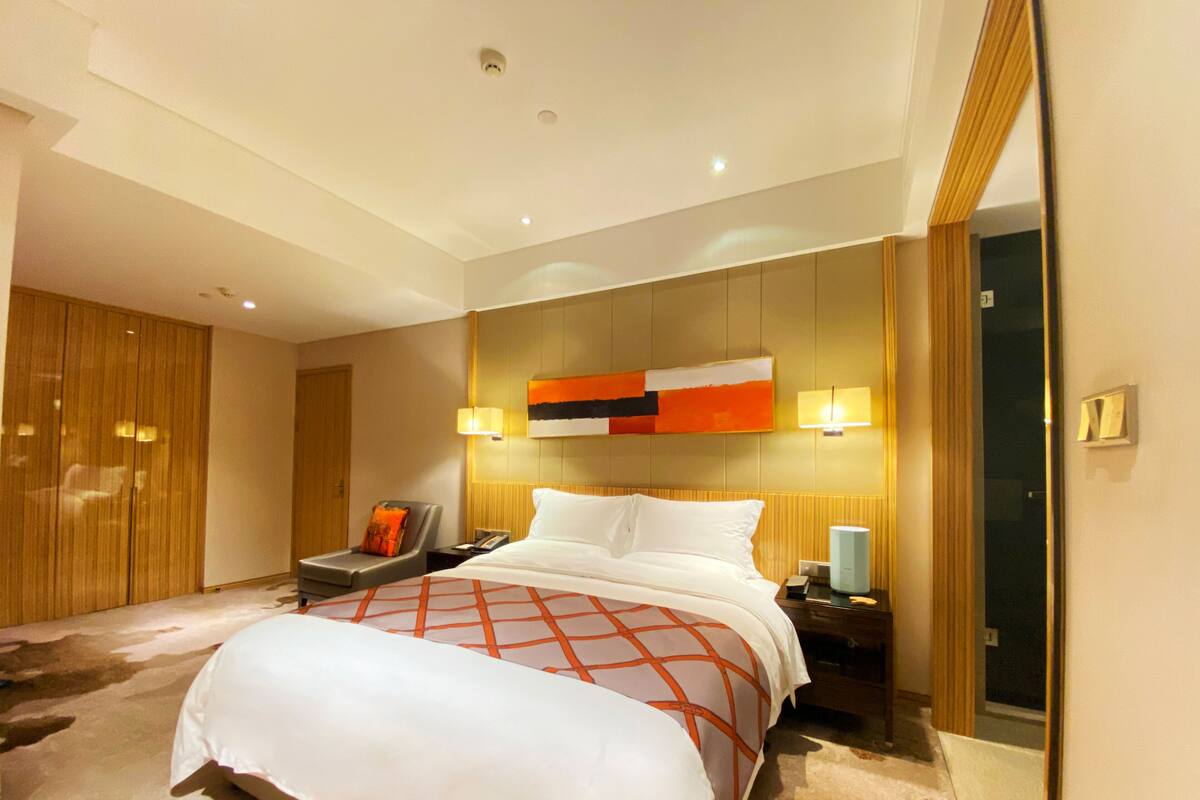 Una habitación de hotel moderna con una cama grande, una mesita de noche, una silla y un espejo.