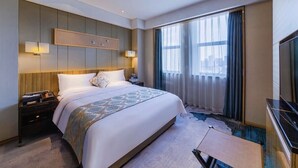 Una habitación de hotel con una cama grande, mesitas de noche, un televisor de pantalla plana y un ventanal con cortinas.