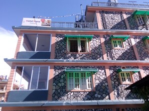 A multi-story building with a stone facade, green window frames, and a sign indicating it is a hotel.