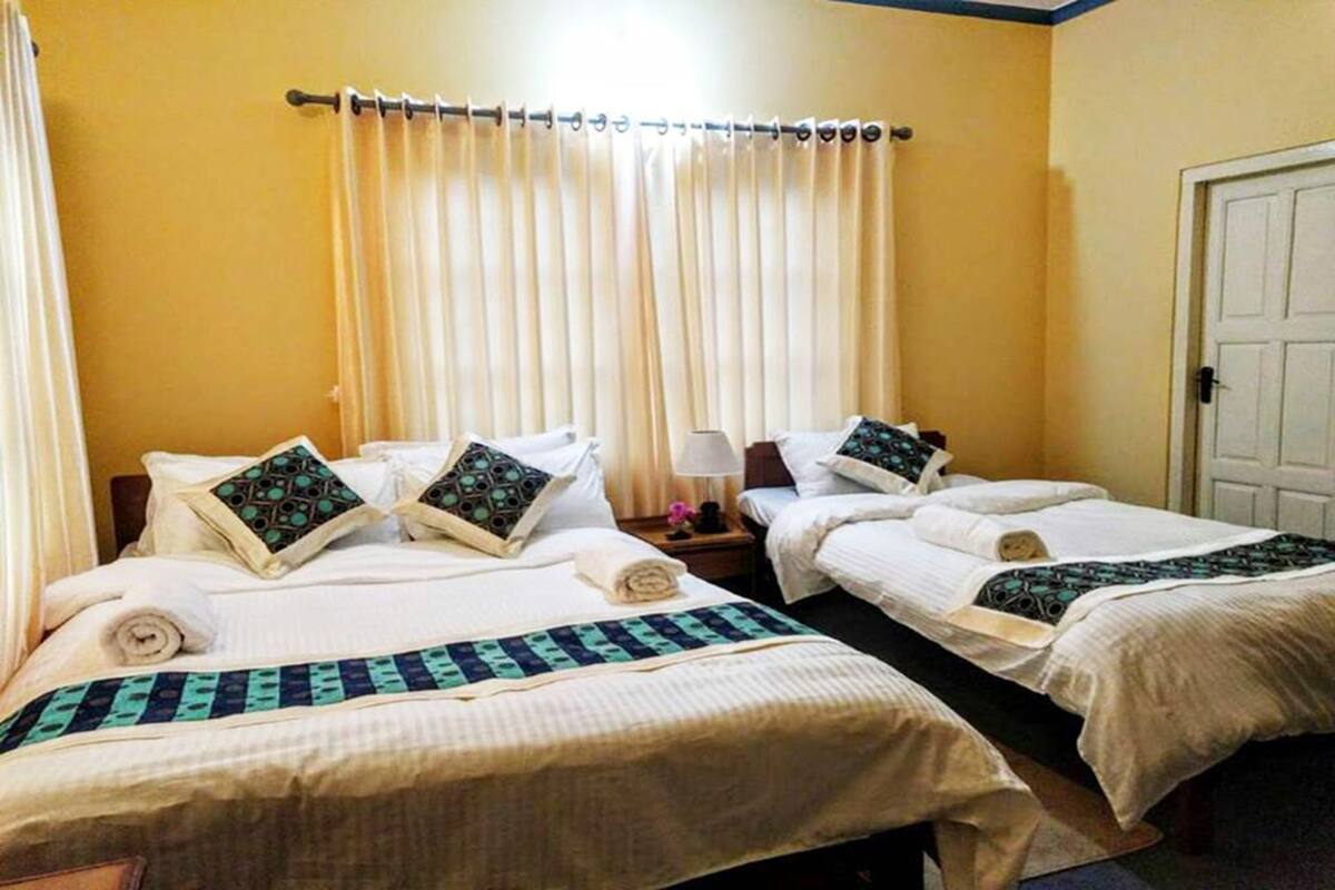 Une chambre d’hôtel avec deux lits, chacun recouvert d’une courtepointe blanche et agrémenté d’oreillers assortis, une table de chevet avec une lampe et une tringle à rideaux au-dessus des lits.