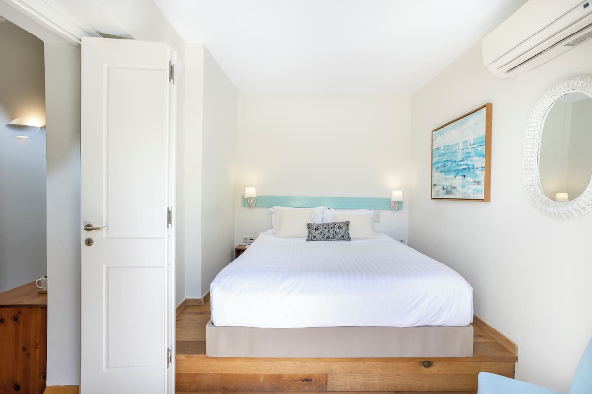 Un dormitorio con cama, mesita de noche, espejo en la pared y un cuadro.