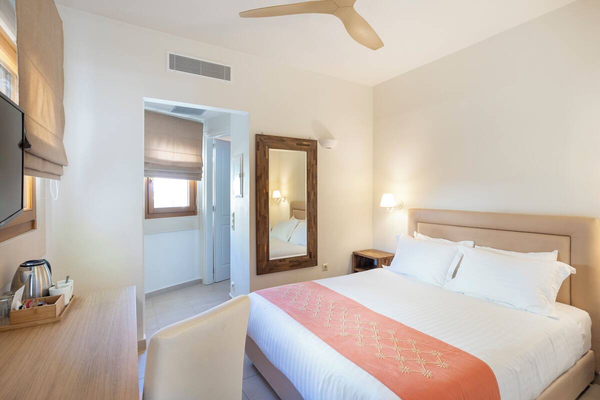 Habitación de hotel con una cama grande, televisión, escritorio con tetera y espejo.