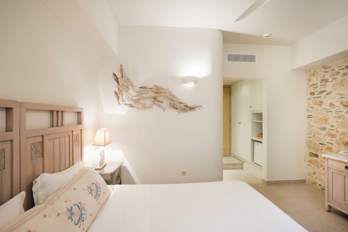 Un dormitorio con cama, mesita de noche, lámpara, pared de piedra y cabecero de madera.