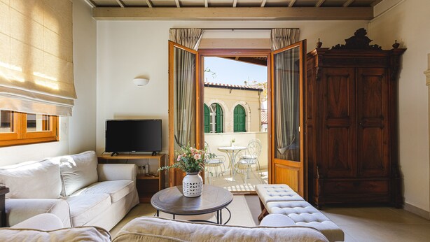 A living room with a sofa, a TV, a coffee table with a vase, and a view of an outdoor patio with a table and chairs. - Z boutique Hotel (Mylopotamos)