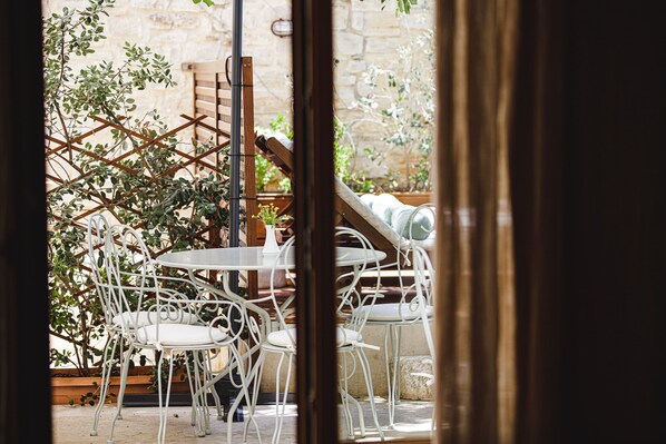 An outdoor seating area with white metal chairs and tables, surrounded by greenery and stone walls. - Z boutique Hotel (Mylopotamos)