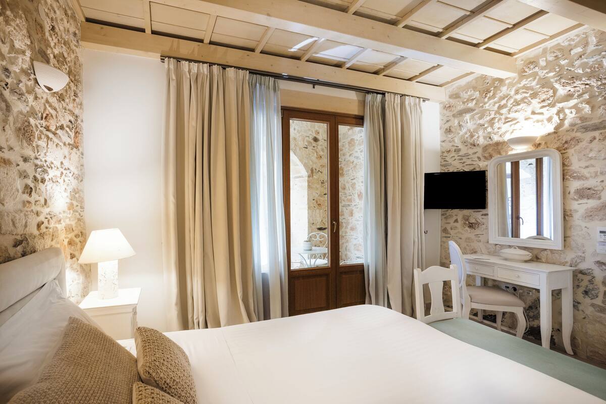 Un dormitorio con cama, escritorio con espejo, silla y ventana con cortinas.