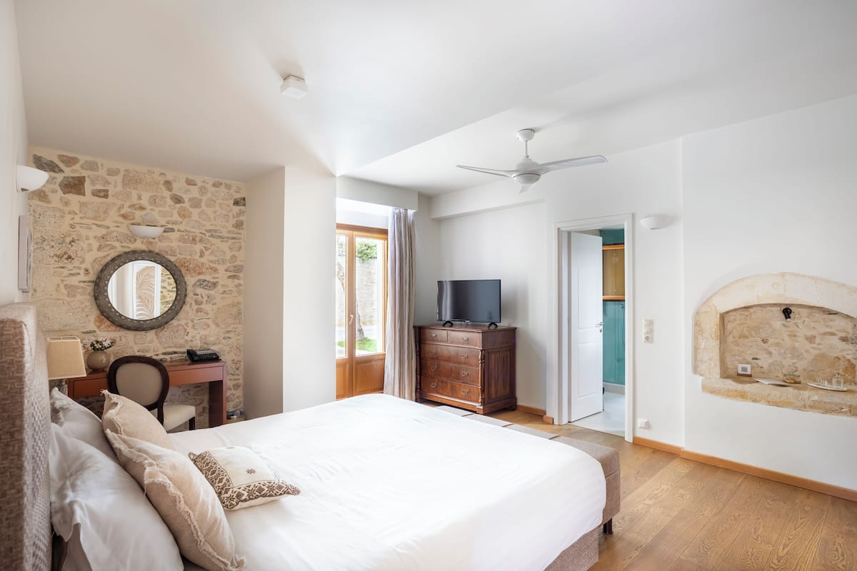 Un dormitorio con una cama grande, una pared de piedra, un aparador de madera, un televisor y una chimenea.