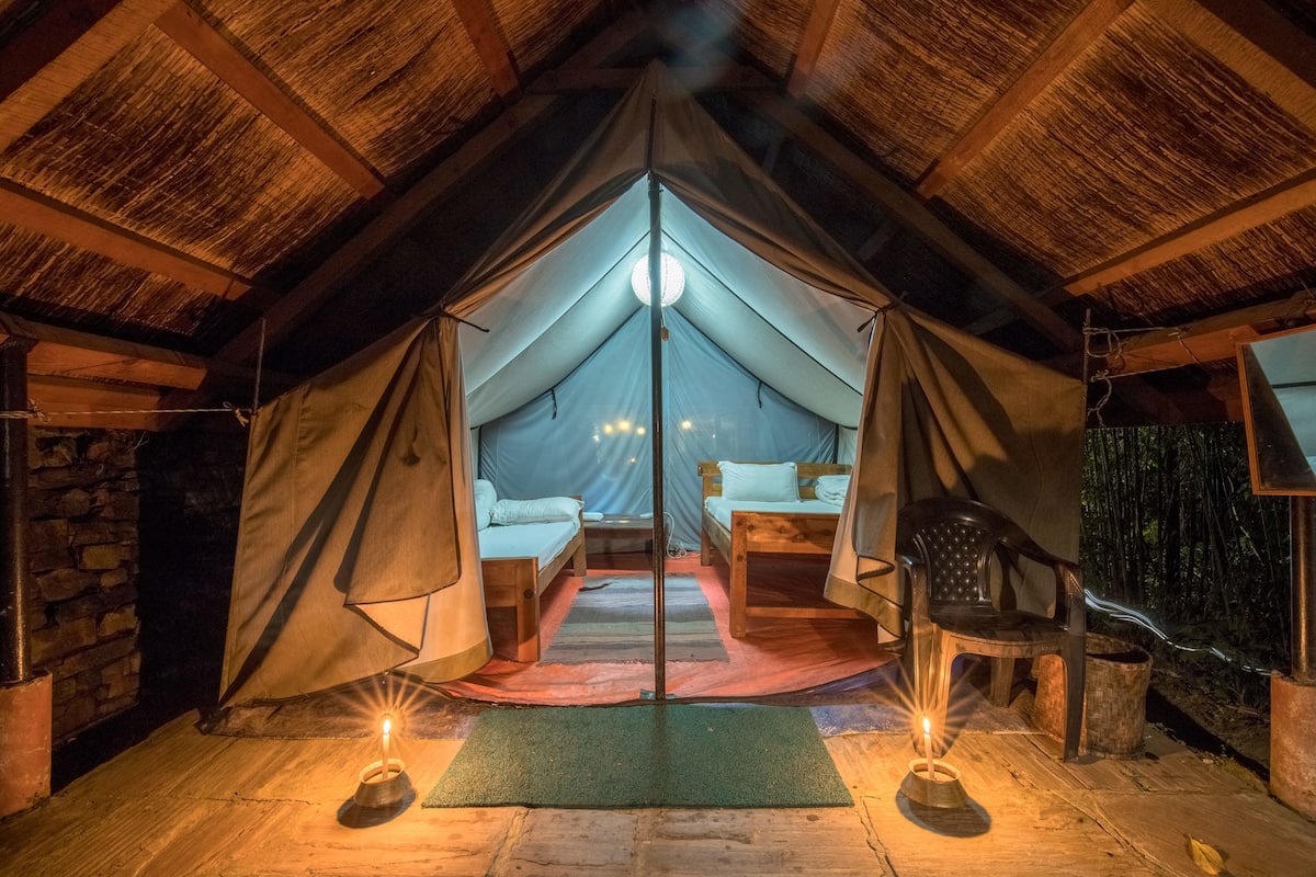 A tented accommodation with two wooden beds, a central table, and a chair.