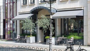 A hotel with a modern facade, outdoor seating, and a bicycle parked outside. - The Midtown Hotel by The New Yorker (Cologne)