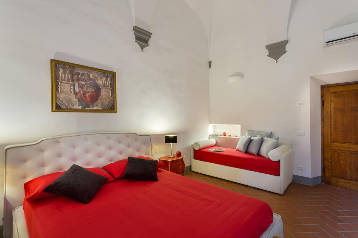 Une chambre avec un grand lit, un petit canapé, une porte en bois et une œuvre d’art au plafond.