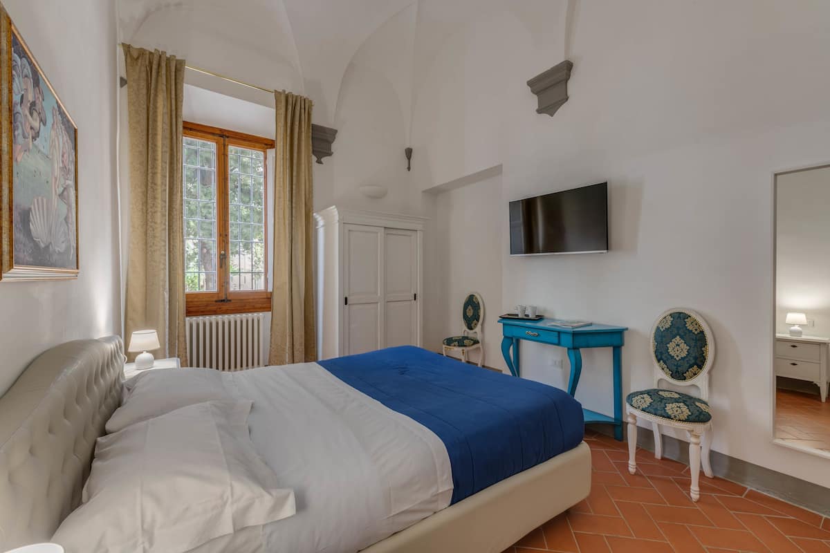Une chambre à coucher avec un lit, un bureau, des chaises, une télévision et une fenêtre avec des rideaux.