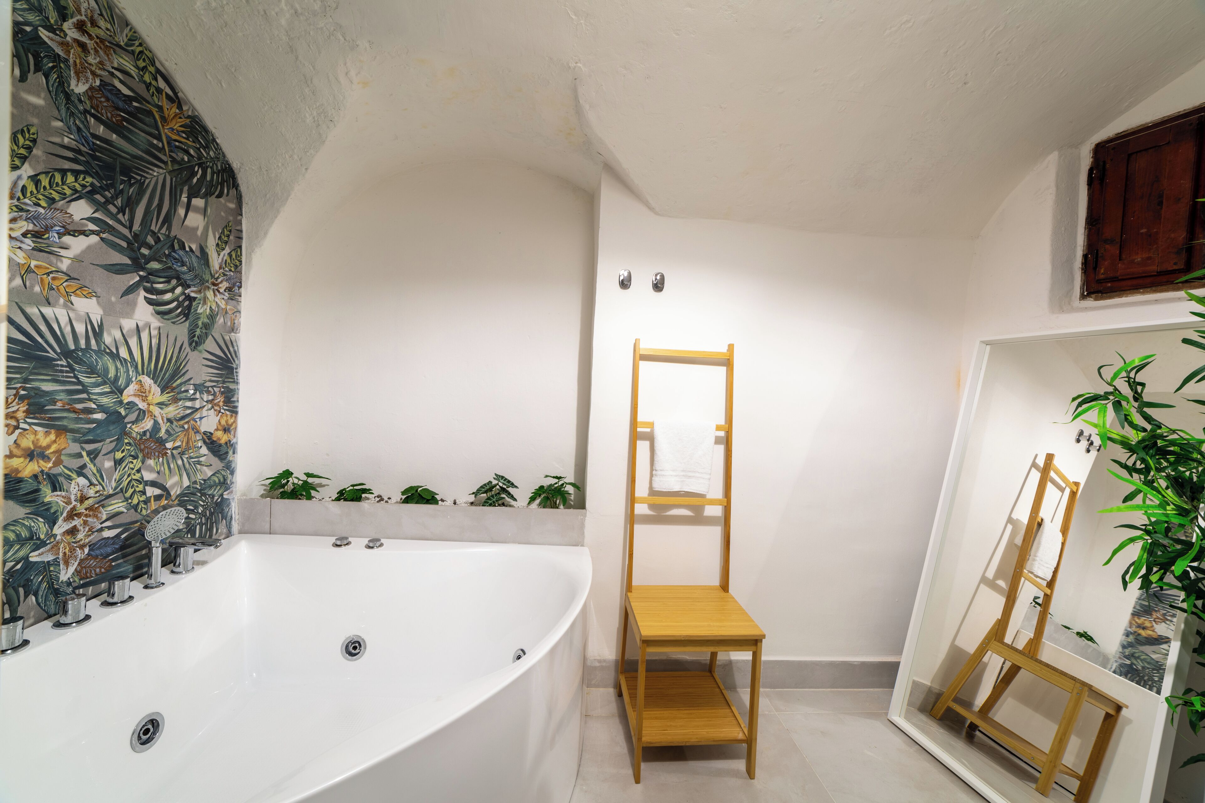 A bathroom with a freestanding bathtub, a wooden chair, a mirror with a wooden frame, and a potted plant.