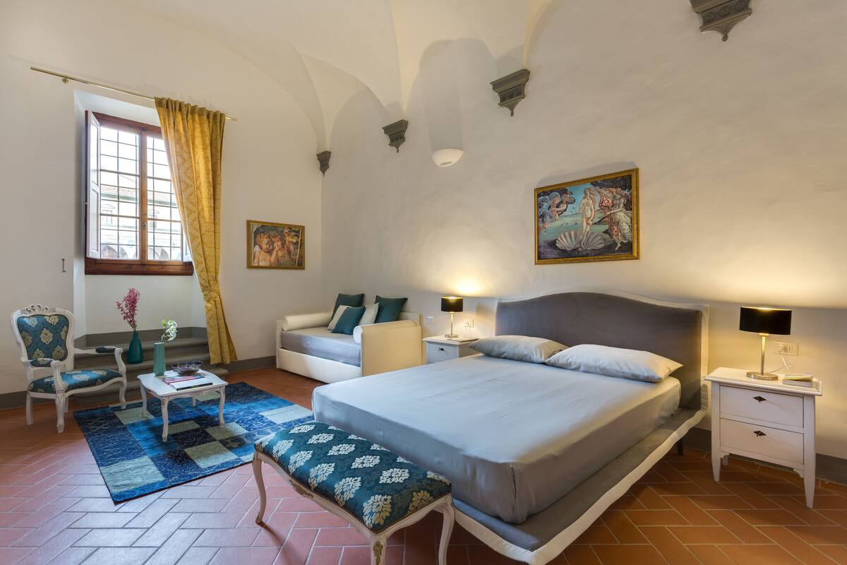 Une chambre à coucher avec un lit, des tables de chevet, une chaise, un canapé et une fenêtre avec des rideaux.