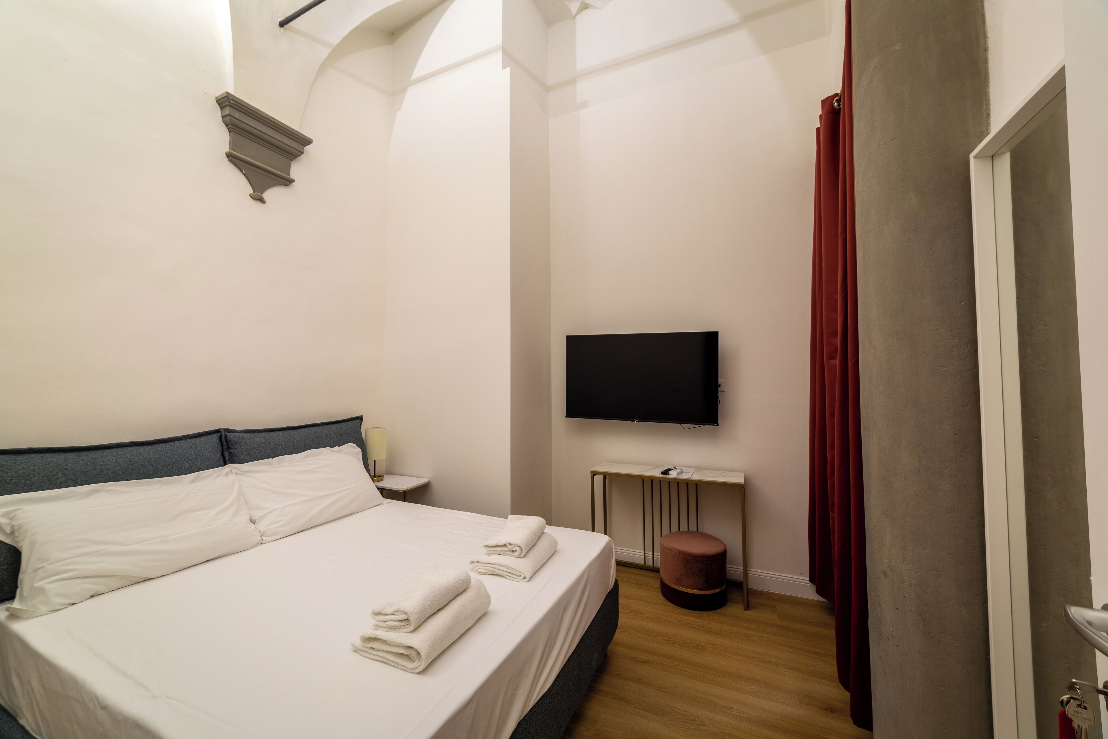 Habitación de hotel con cama, televisión, una mesita y una cortina roja.