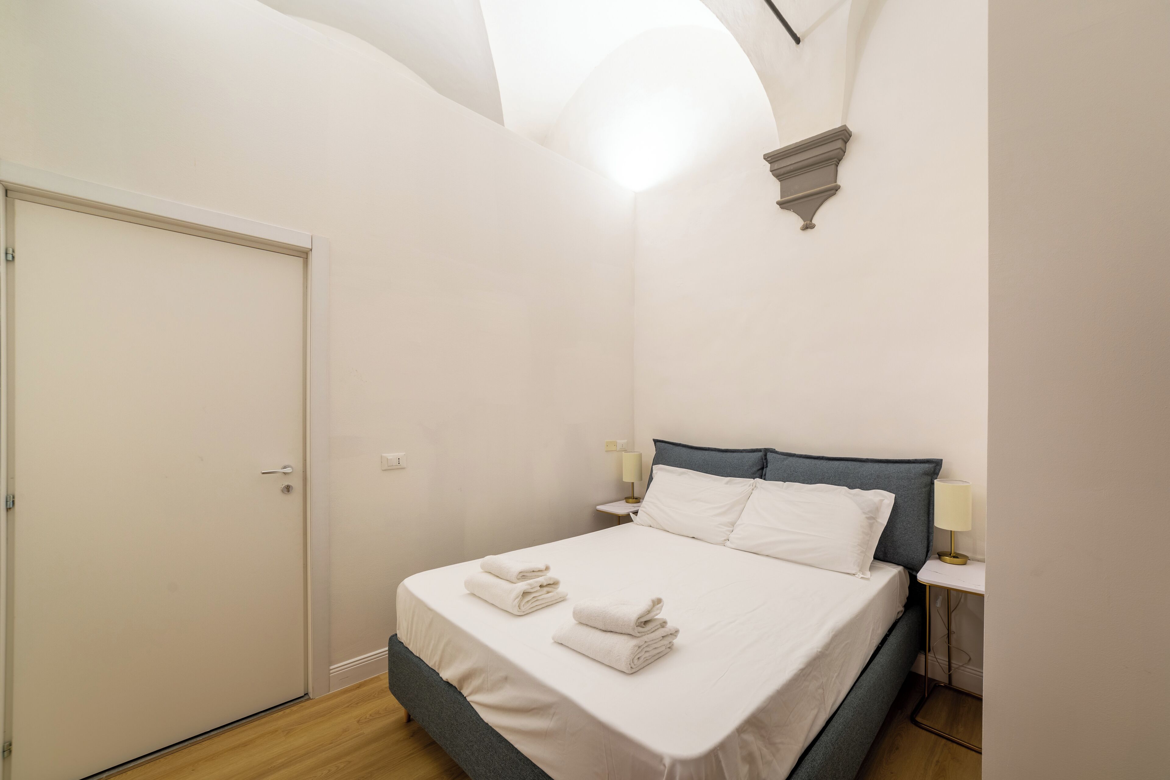 A bedroom with a bed, bedside tables, and a door.