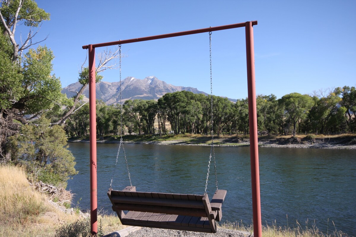 A wooden swing set by a lake with a mountain in the background.