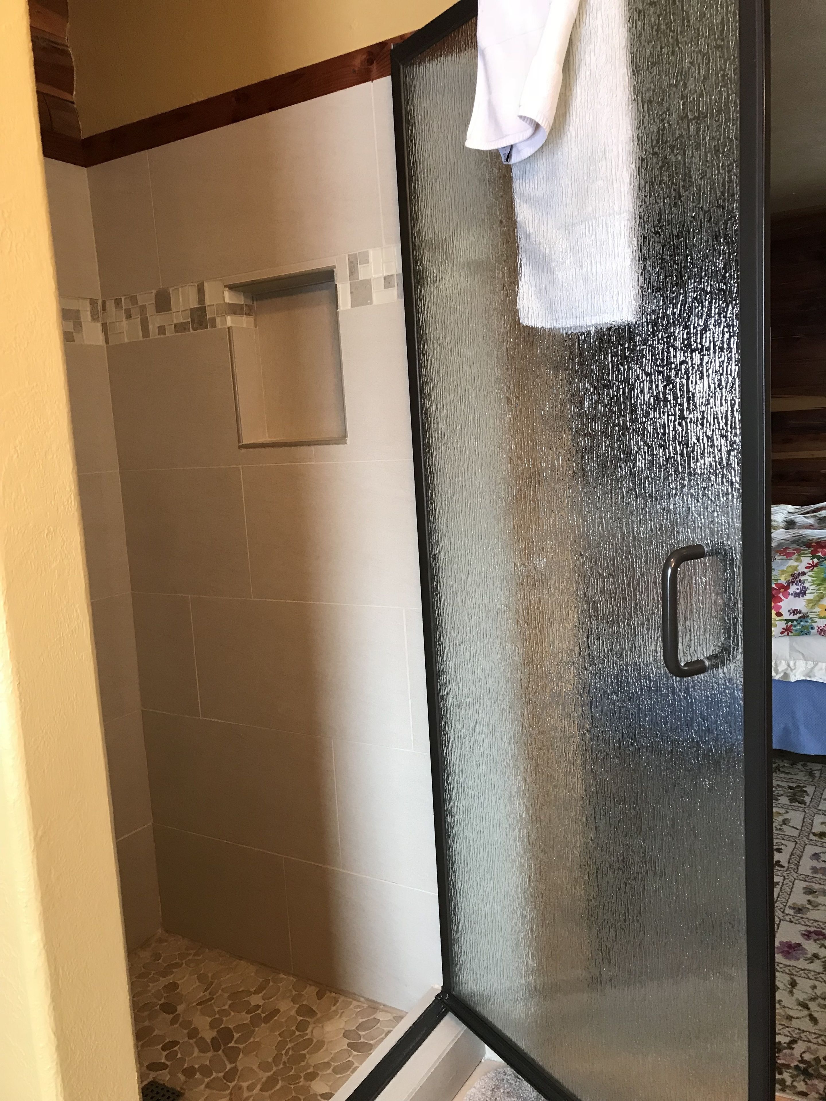 Une douche fermée par des parois de verre, avec une serviette blanche accrochée à la porte.