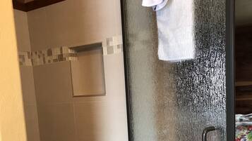 Une douche fermée par des parois de verre, avec une serviette blanche accrochée à la porte.